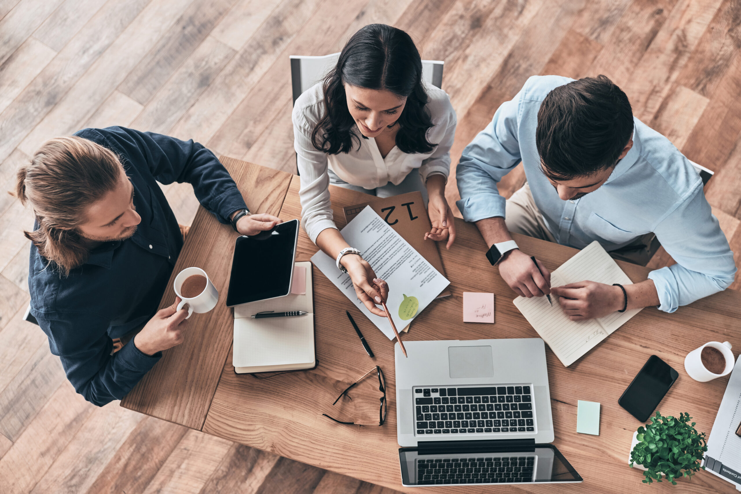 Talking about business details. Top view of young modern colleagues in smart casual wear working together while spending time in the office